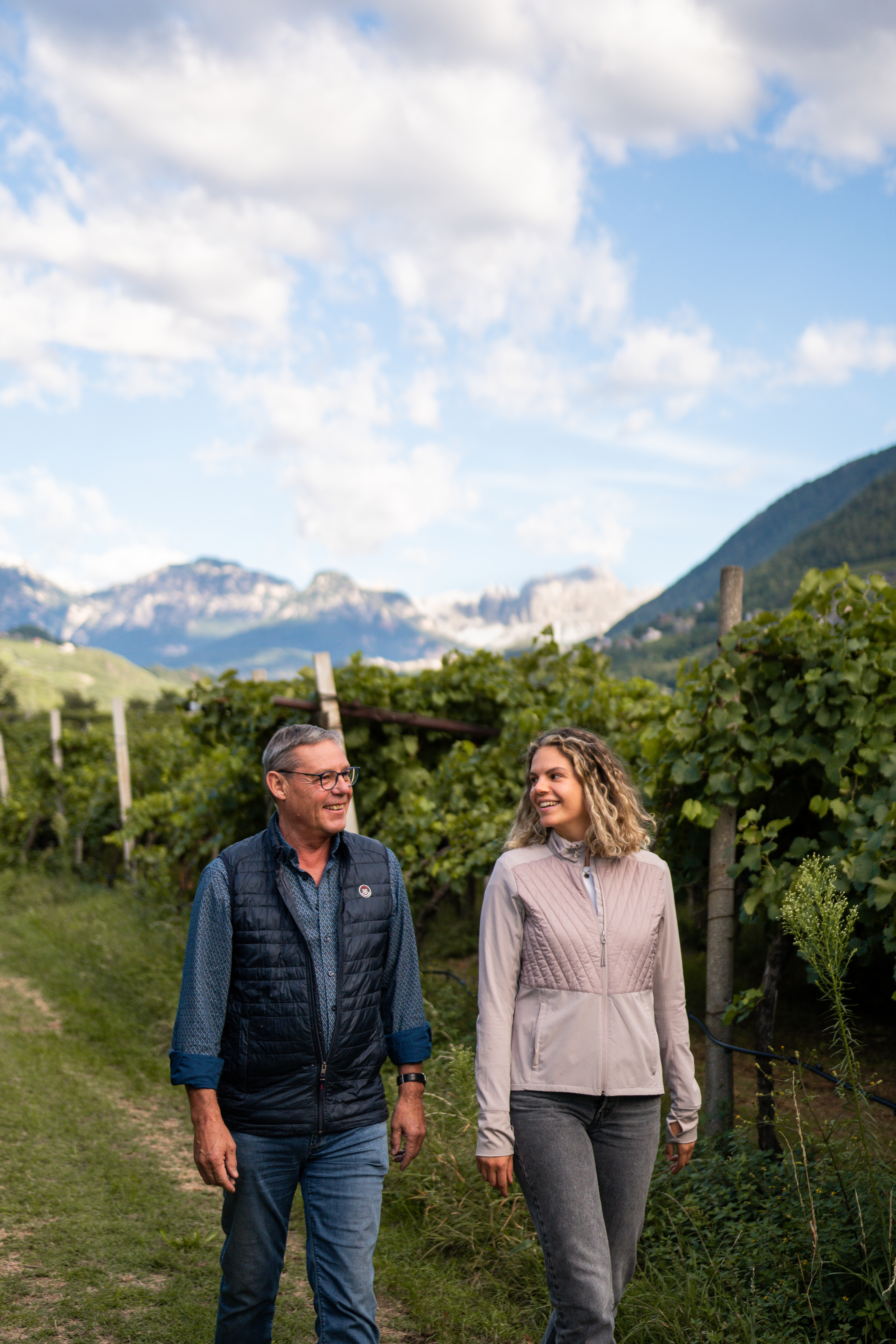 Due membri della famiglia Pfeifer passeggiano tra i vigneti a pergola del Pfannenstielhof, sullo sfondo le montagne